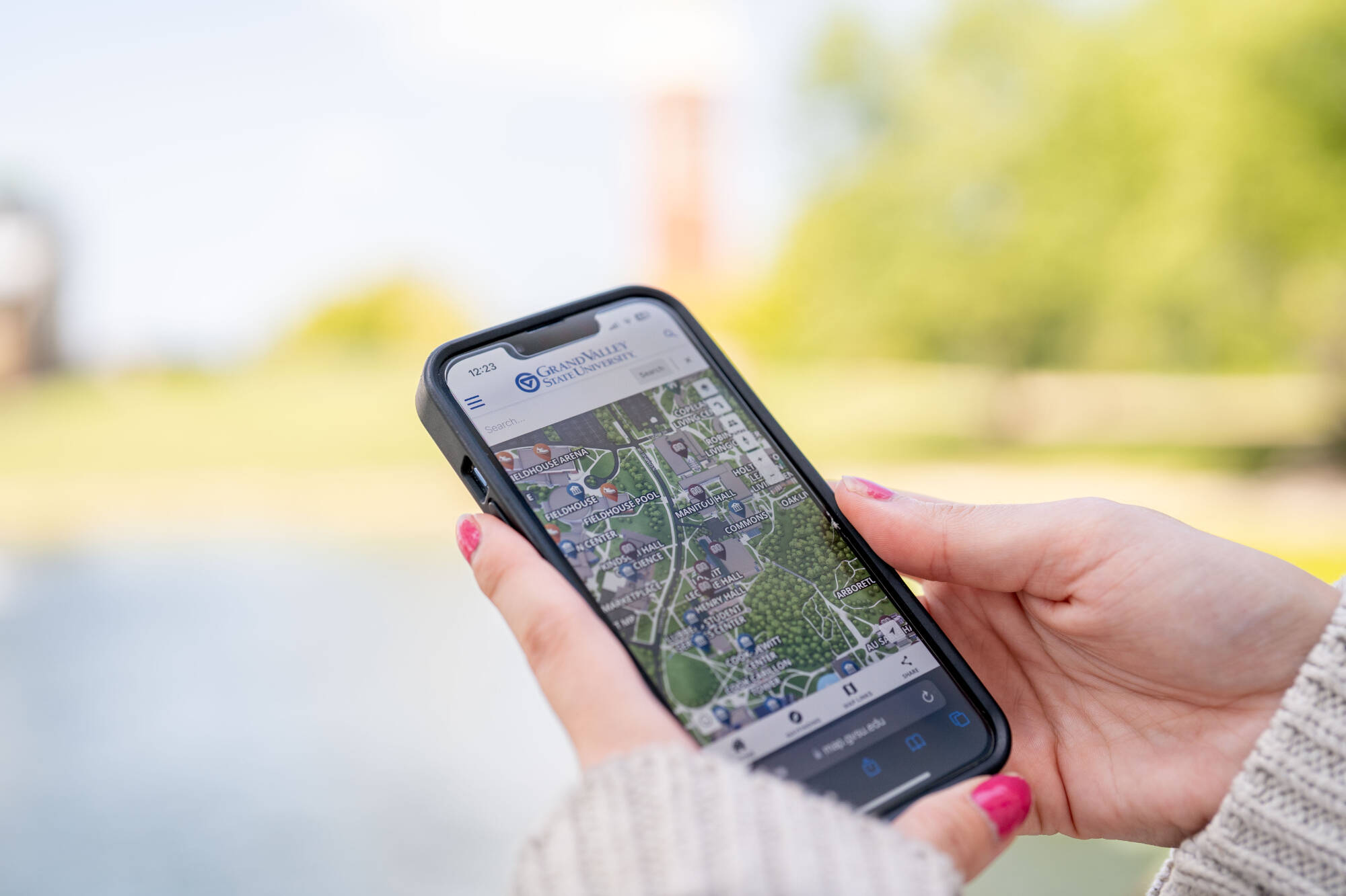 Person holding a smartphone displaying a map app with a blurred park in the background.